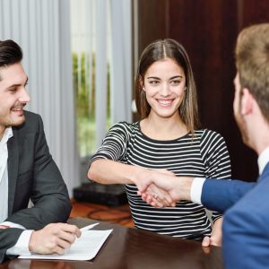 Smiling young couple shaking hands with an insurance agent